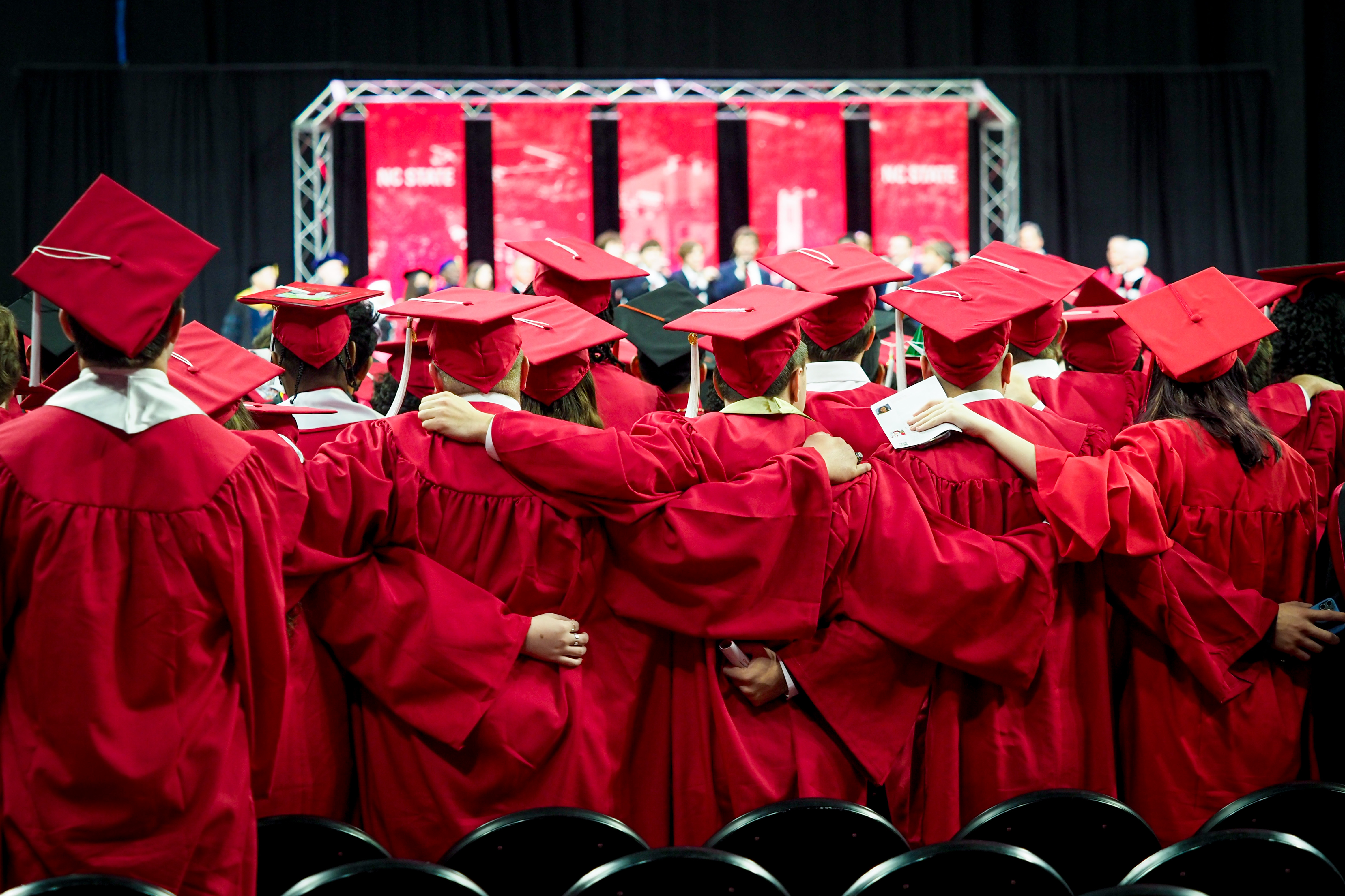 A group of graduates in cap and gown embrace eachother during the commencement ceremony
