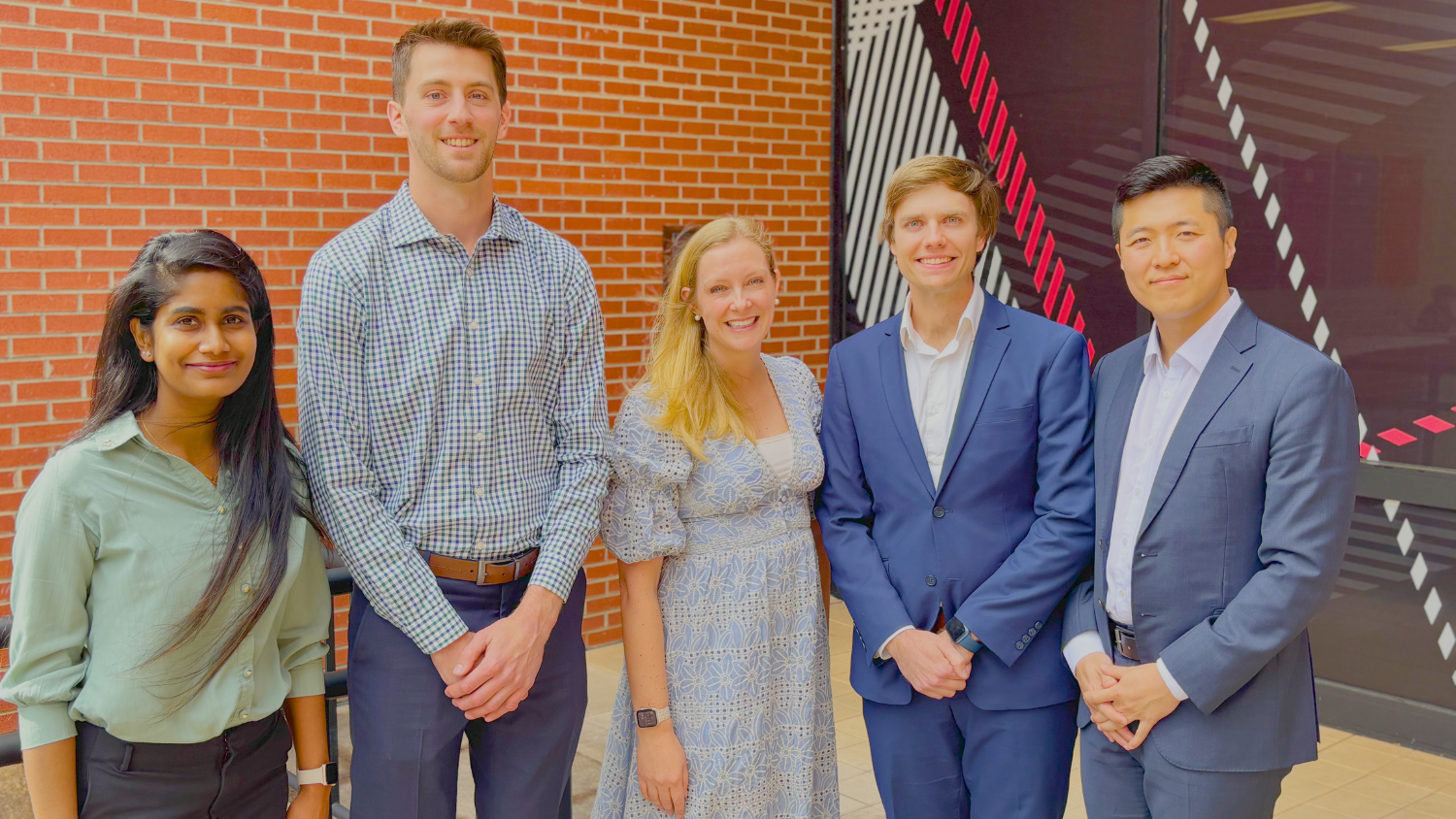 Image shows 5 people all standing next to each other smiling.