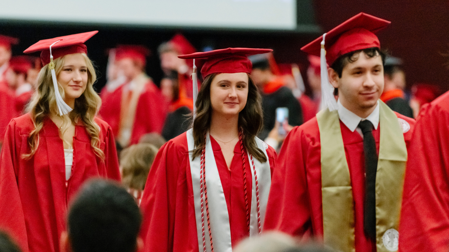 A photo of graduates walking on graduation day. They are wearing red caps and gowns