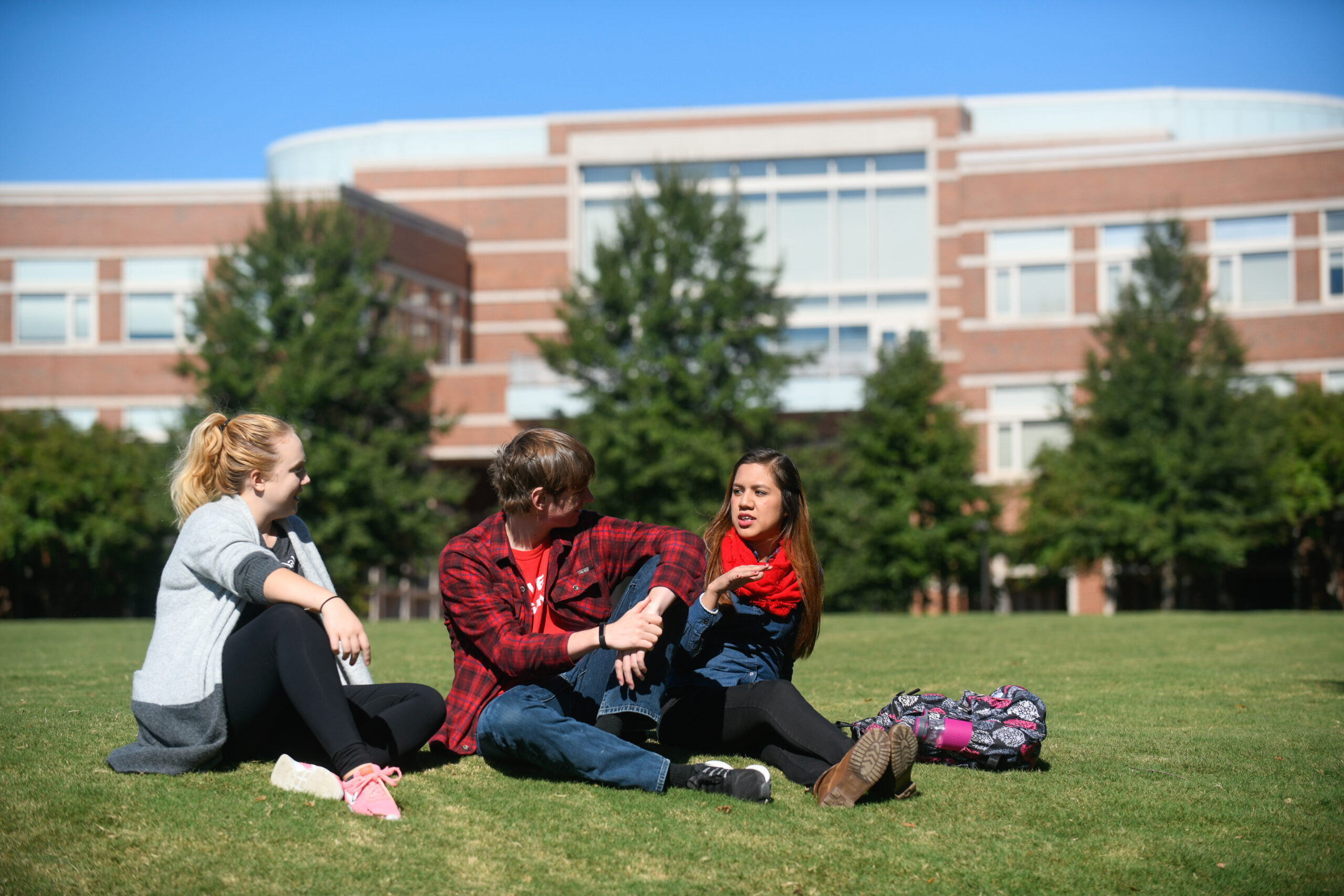 Image shows three students sitting on the lawn at NC State's campus