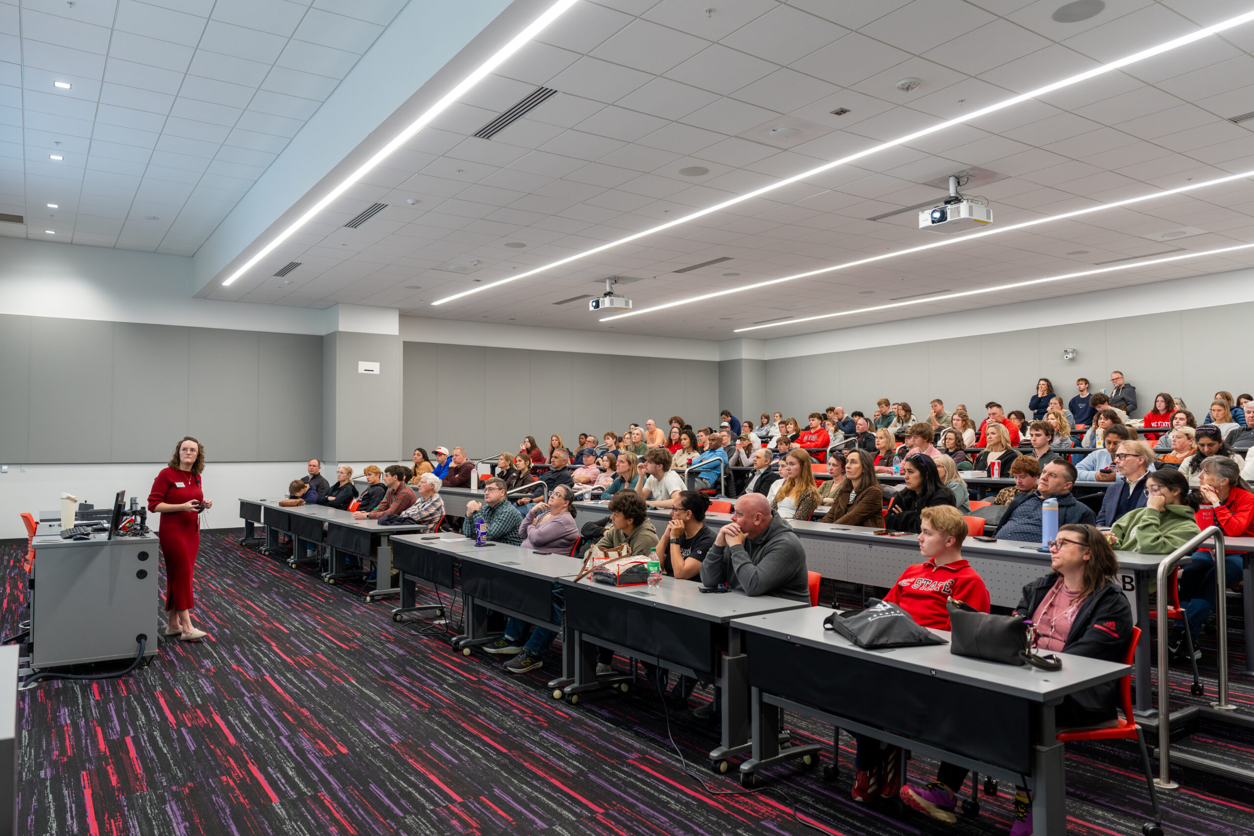 Image shows a crowded lecture room with a professor at the front.